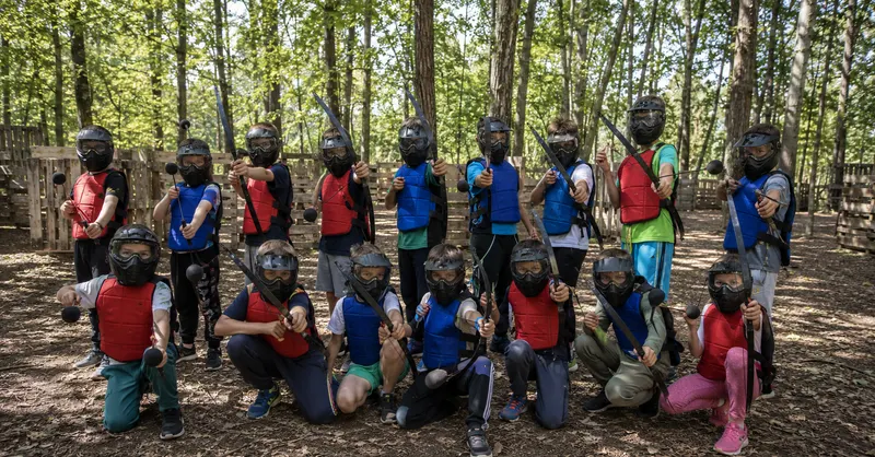 Groupe d'enfants en tenue de jeu, masque intégral sur le visage, posant après une partie d'Archery Tag en forêt