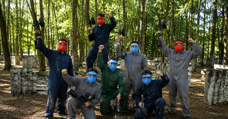 Groupe d'adultes en tenue de jeu, masque sur le visage et équipement en main, célébrant la fin d'une partie en forêt